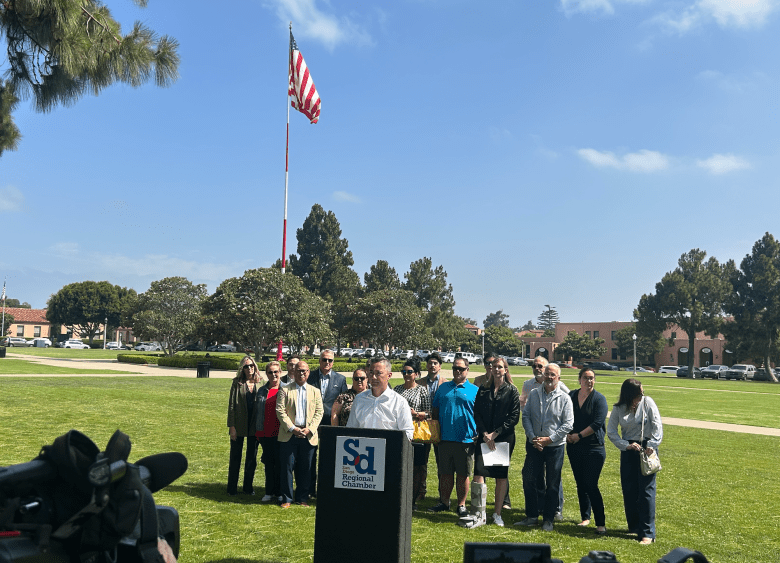 People gather at a podium in a park to discuss objections to a San Diego minimum wage proposal.